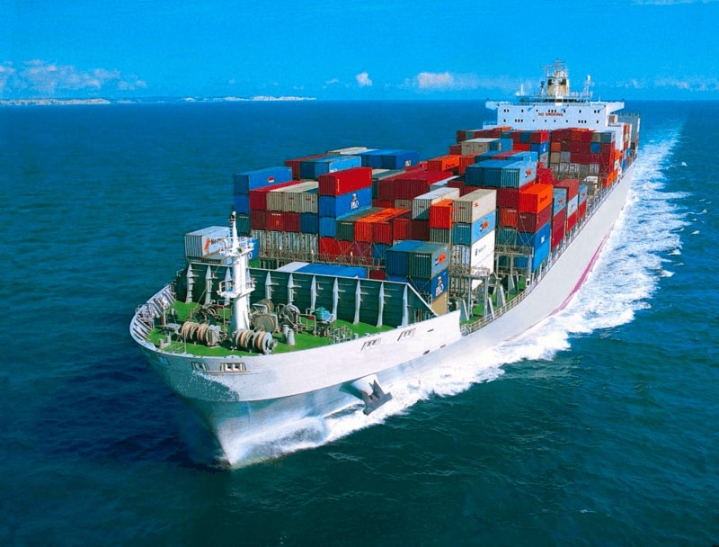 white container ship moving on ocean carrying red, white & blue intermodal containers